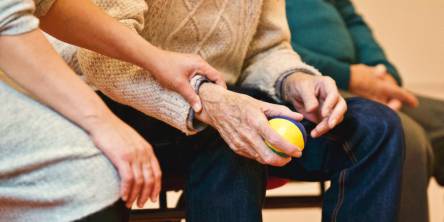 Three people sitting on a a bench. Two are elderly men and one is a woman. The middle man is holding a stress ball while the woman has her hand on his wrist.